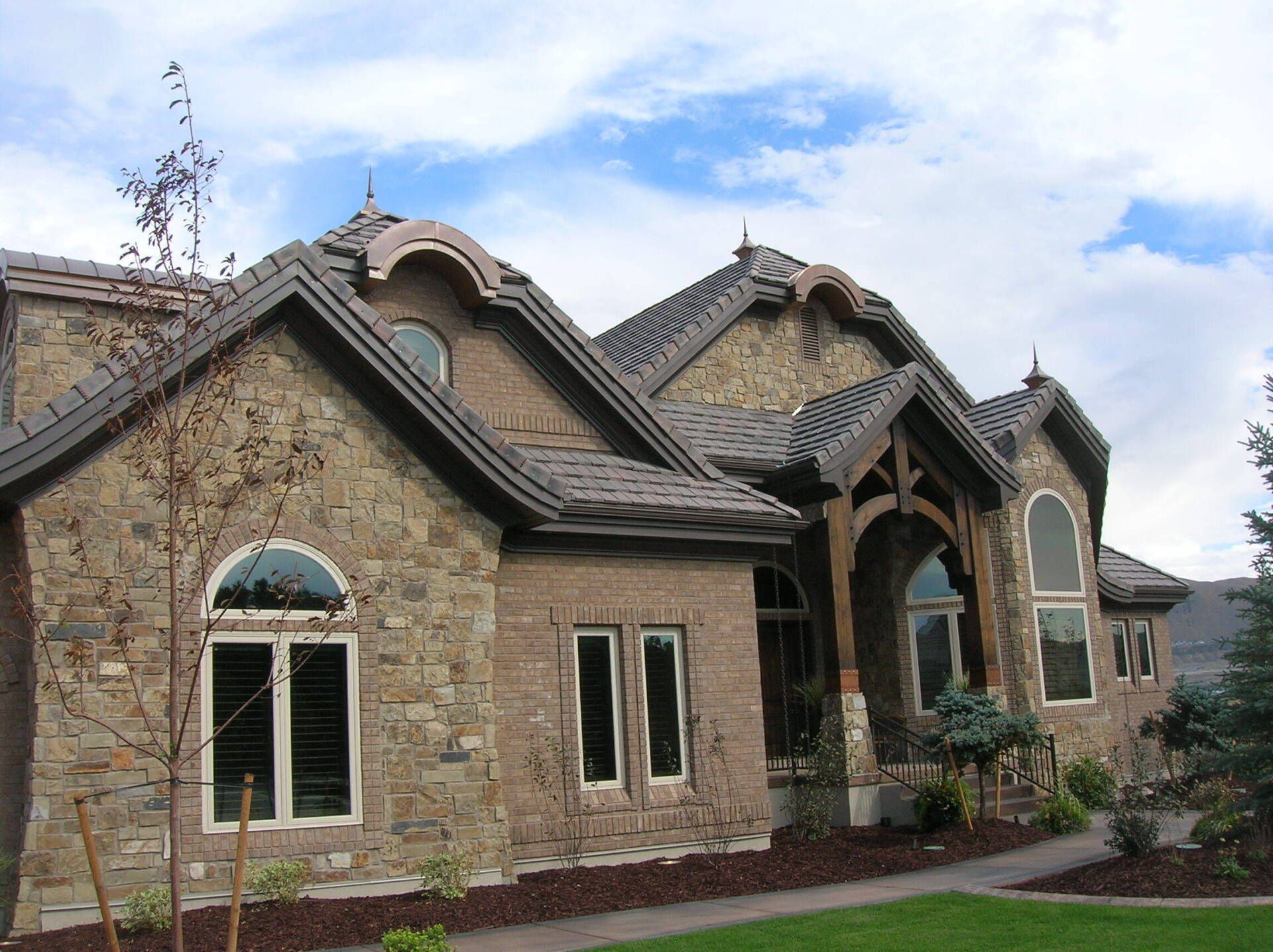 Stone-clad house with dark roof, arched entryway, and arched windows against a cloudy blue sky.