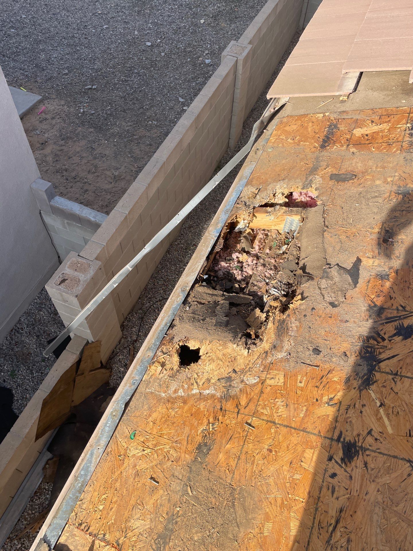 Damaged roof section with rotted wood, showing exposed underlayment and debris.