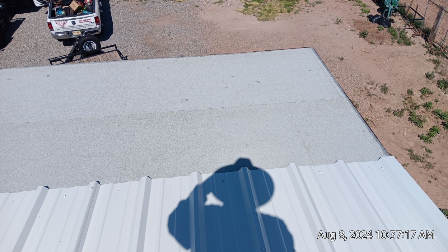 Person's shadow on a metal roof with a truck and equipment in the background. Sunny day.