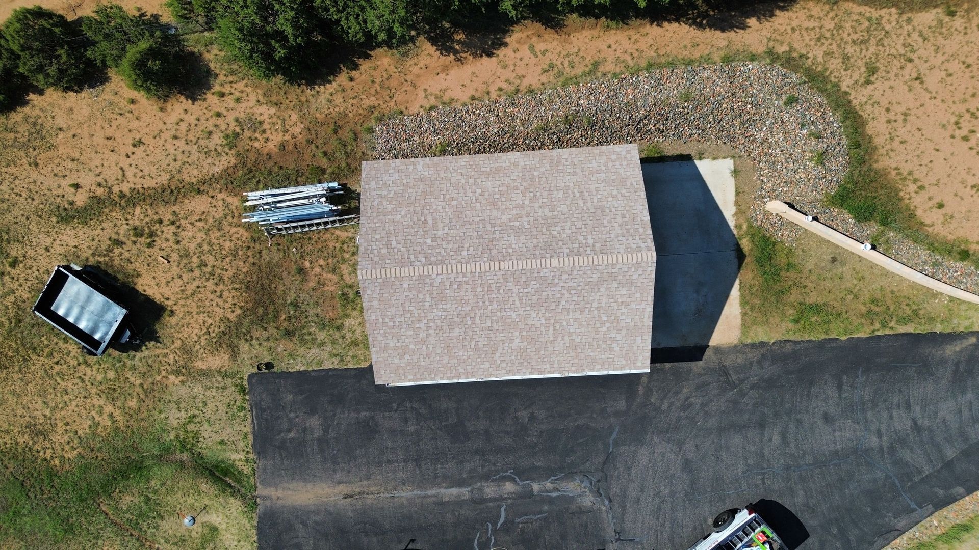 Overhead view of a building with a light brown roof and a black driveway, on a grassy plot.