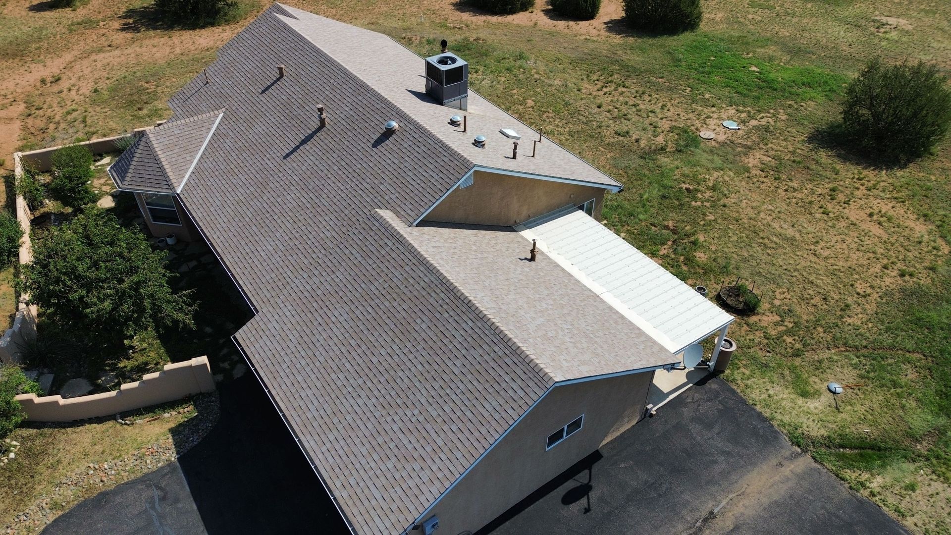 Aerial view of a house with gray shingles, surrounded by greenery and asphalt driveway.
