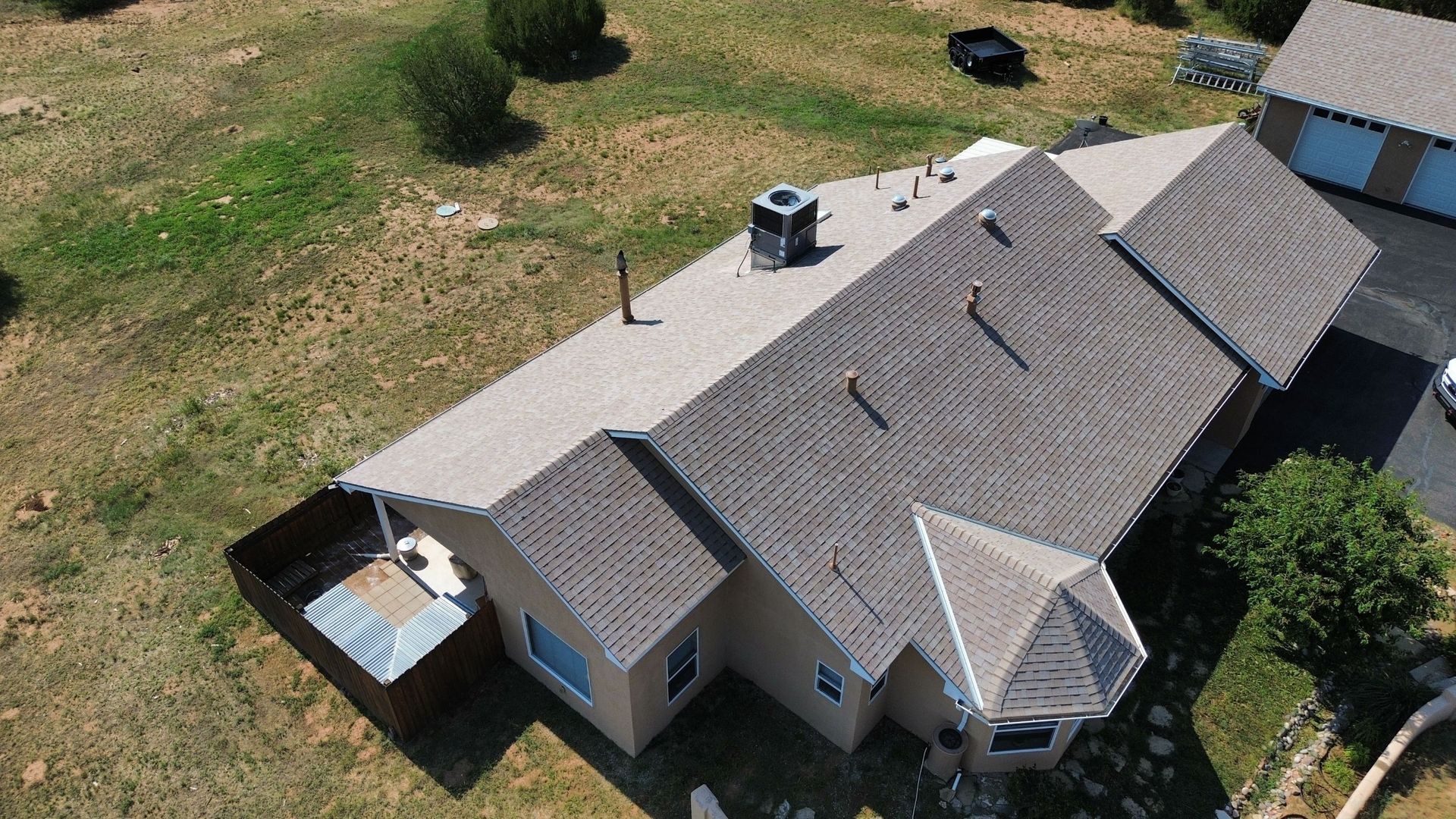 Aerial view of a beige house with a brown roof on a grassy plot of land.