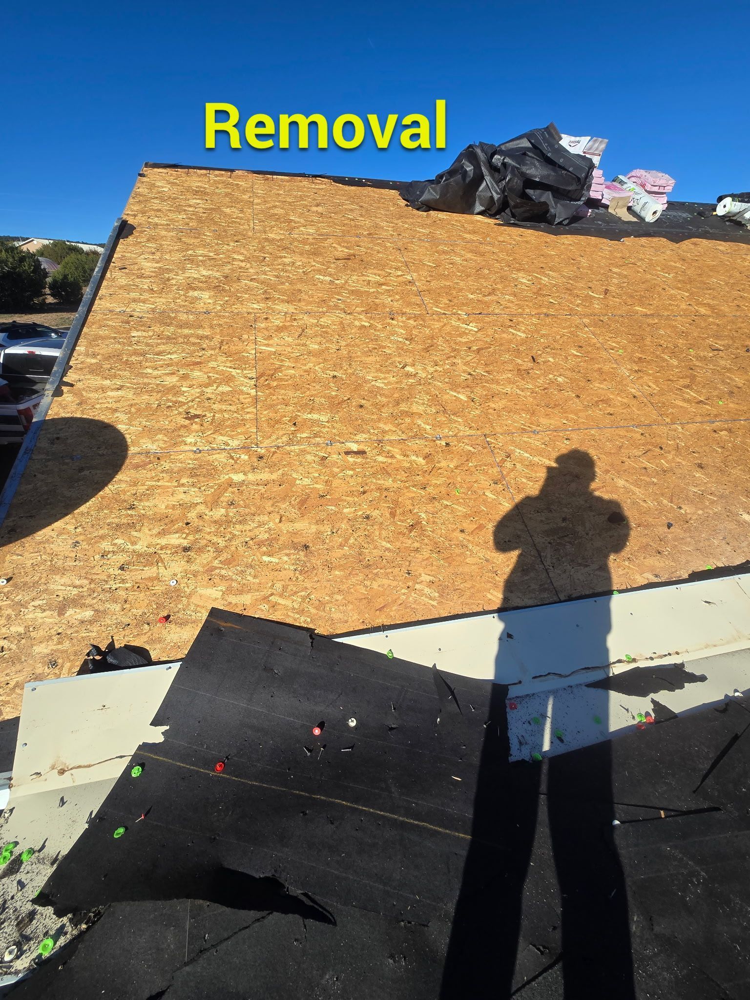 Roof with exposed wood, partial shingle removal, and person's shadow. 