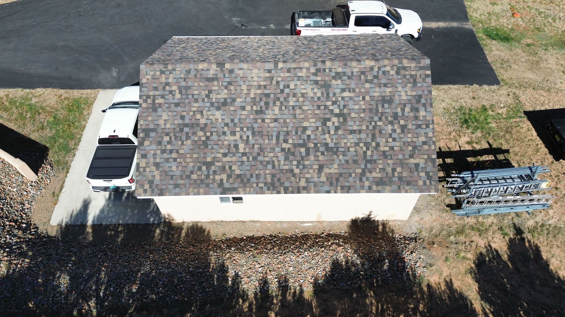 Overhead view of a tan building with a brown roof; two white trucks parked outside.