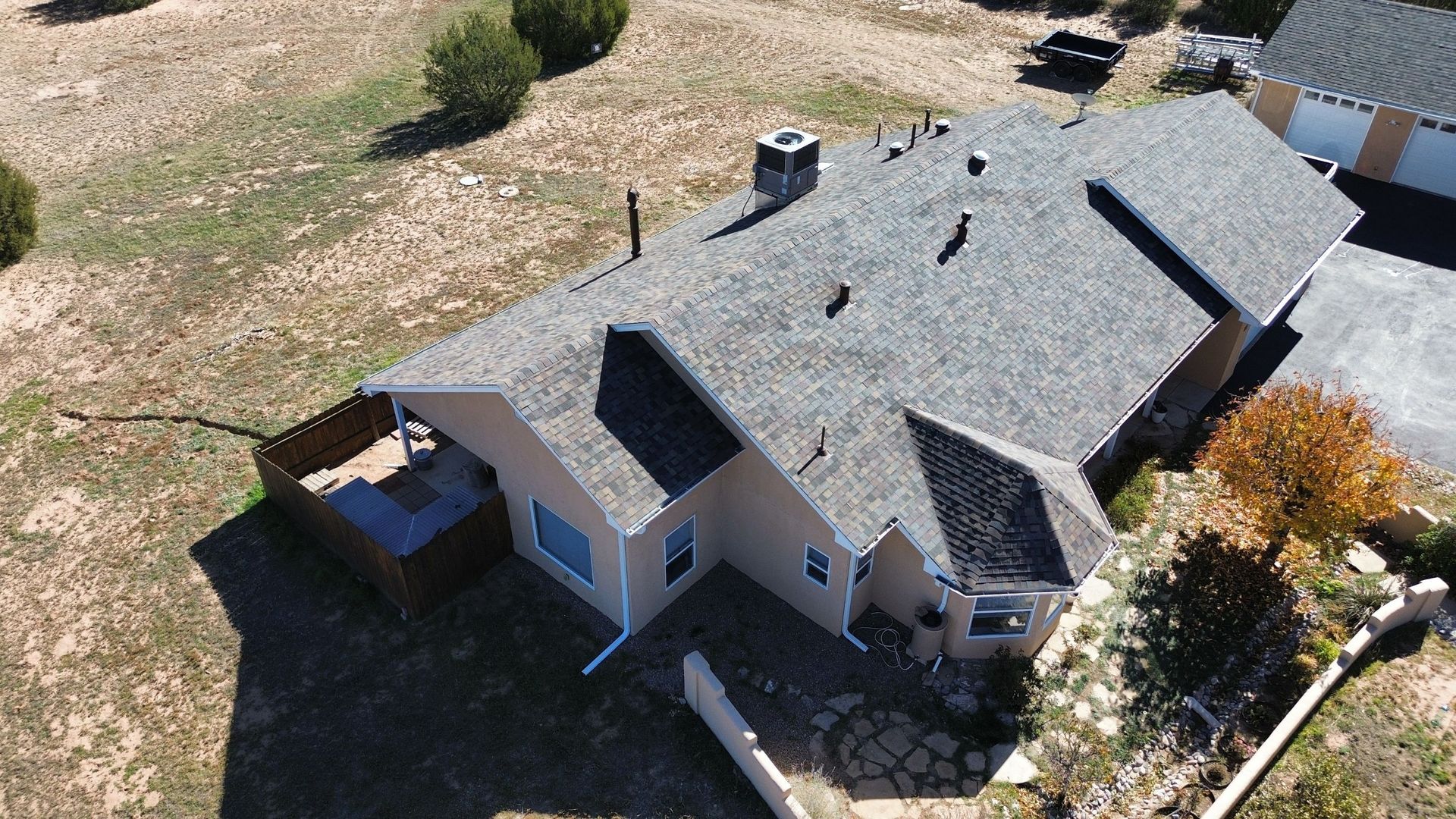 Aerial view of a light brown house with a gray roof and a wooden fence on a sunny day.