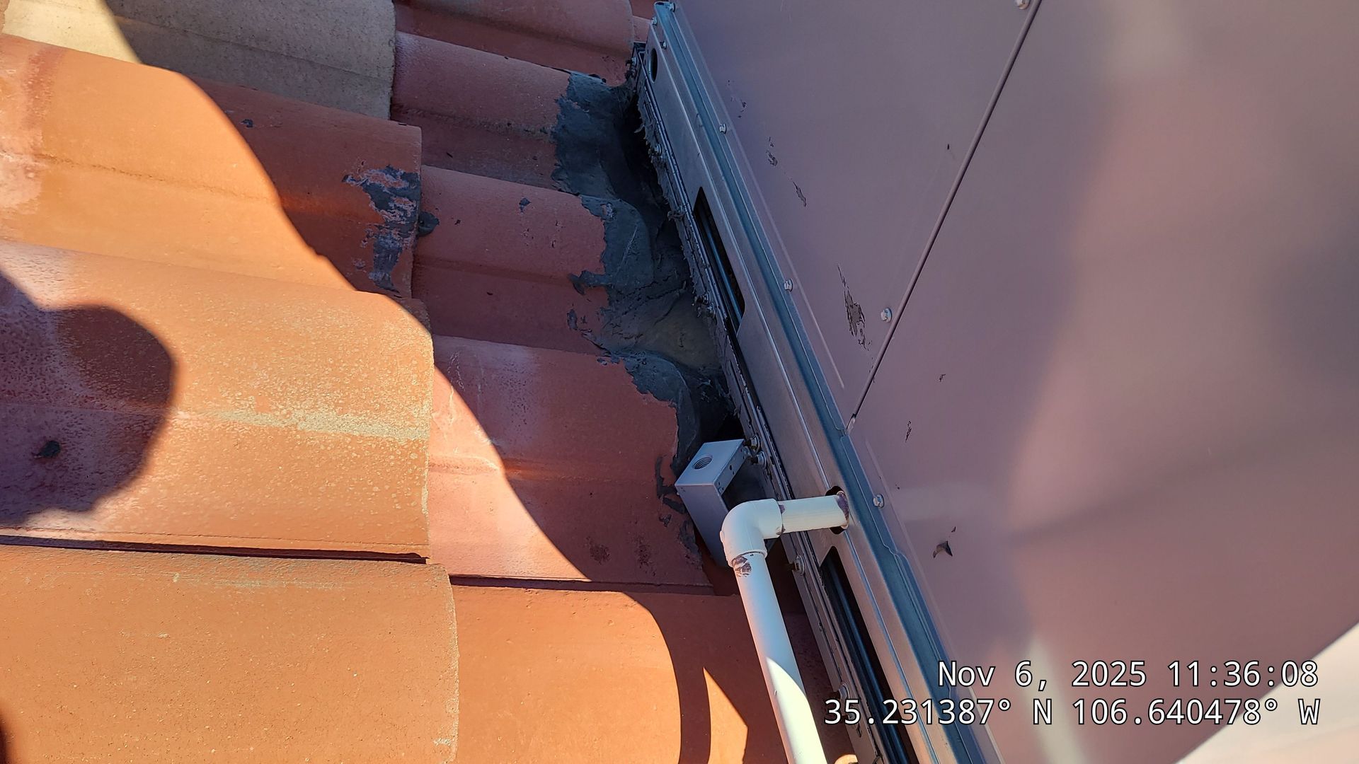 Clay roof tiles and building side with sealant and white pipe.