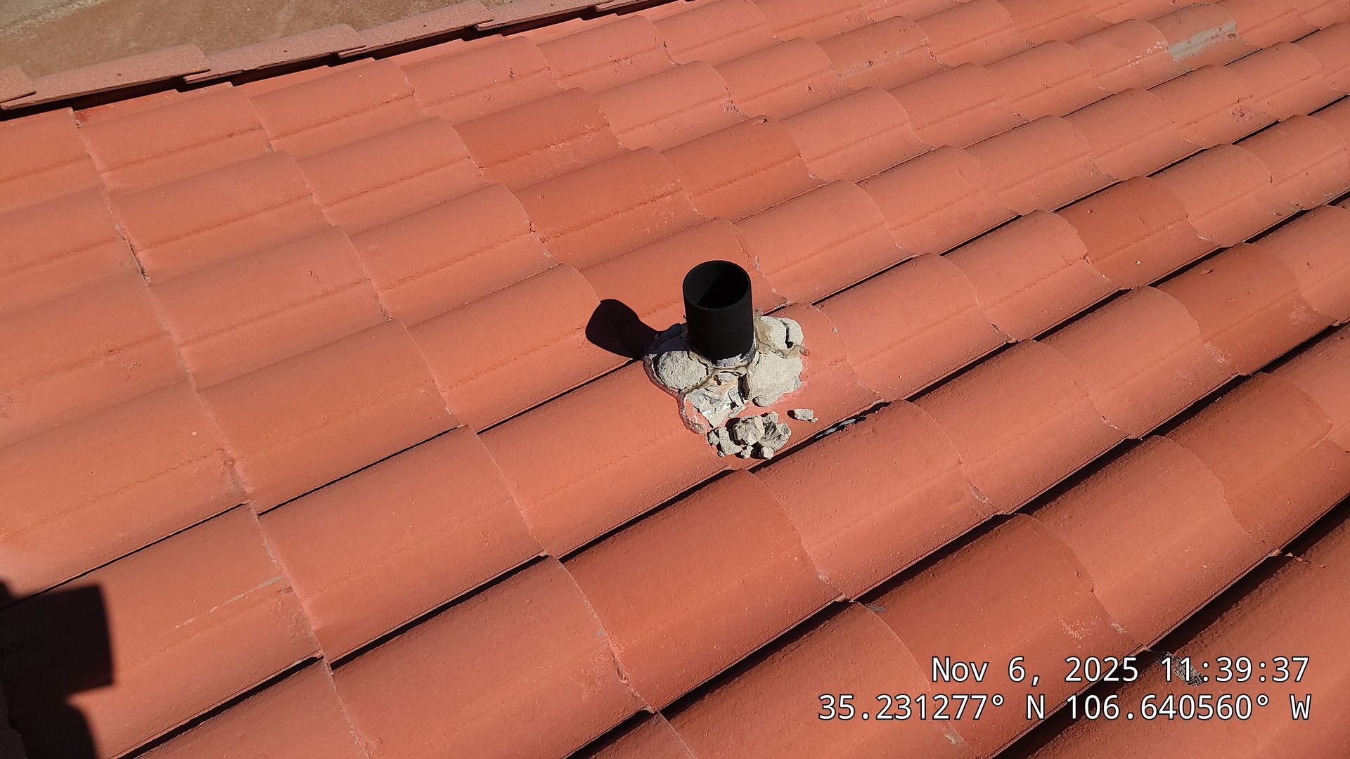 Black pipe protruding from a red tile roof, surrounded by concrete.