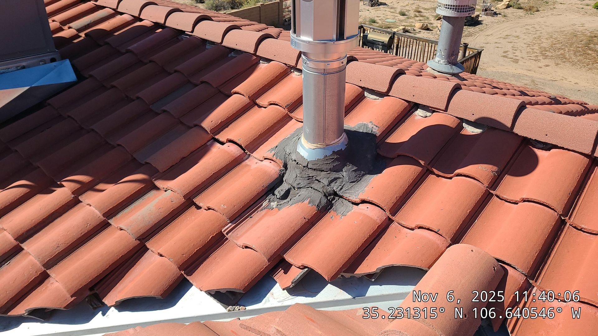 Red tile roof with a metal pipe chimney, sealed with dark gray sealant.