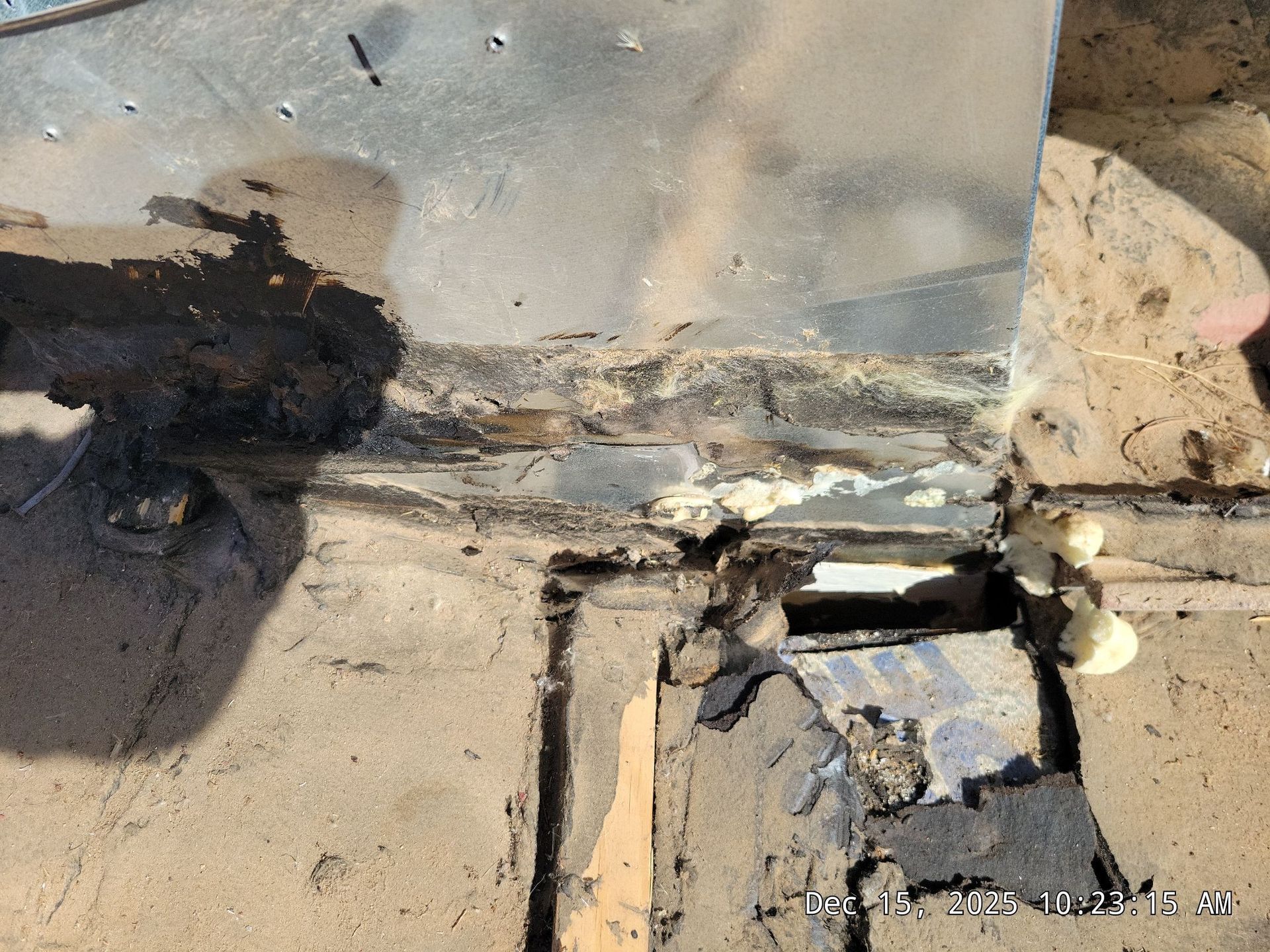 Close-up of a damaged roofing area with metal flashing, tar, and expanding foam visible.