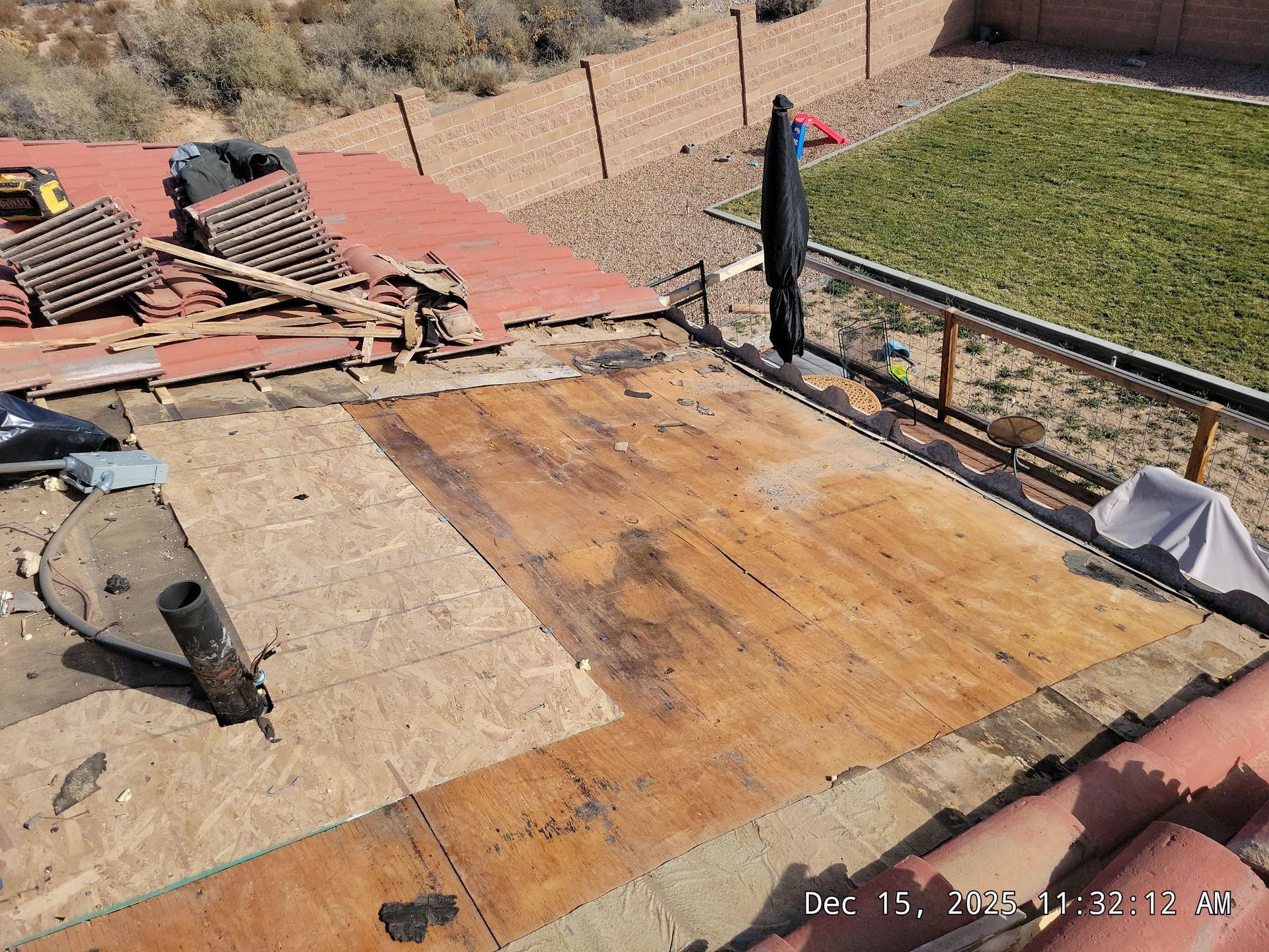 Partially dismantled roof with exposed wood, red tiles, and a backyard view.