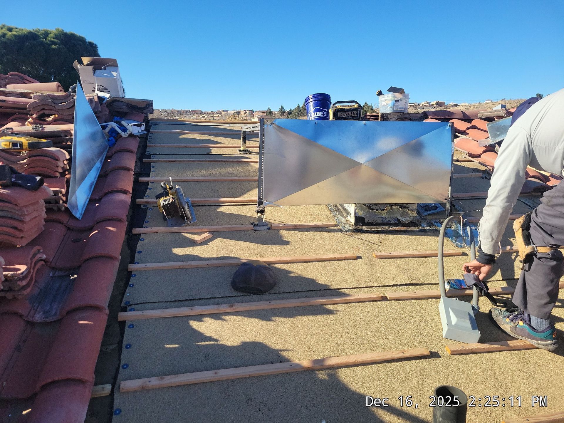 Roofer on a tile roof installs metal flashing. Sunny day, blue sky.