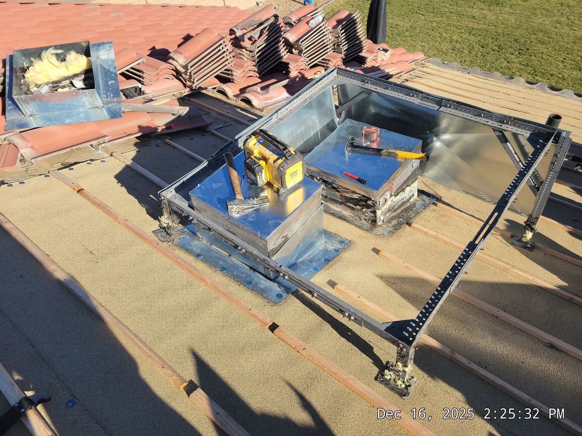 Rooftop scene with metal boxes and tools, possibly HVAC installation. Beige roof with orange tiles.