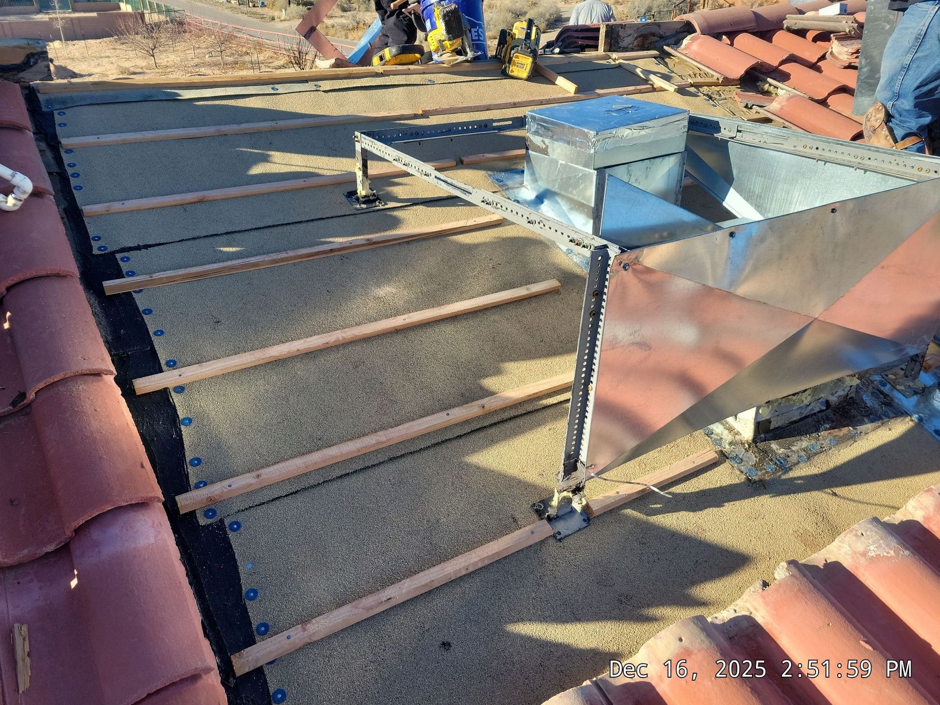 Rooftop ventilation system installation: Metal box on a frame, wooden beams on a textured surface, clay roof tiles.