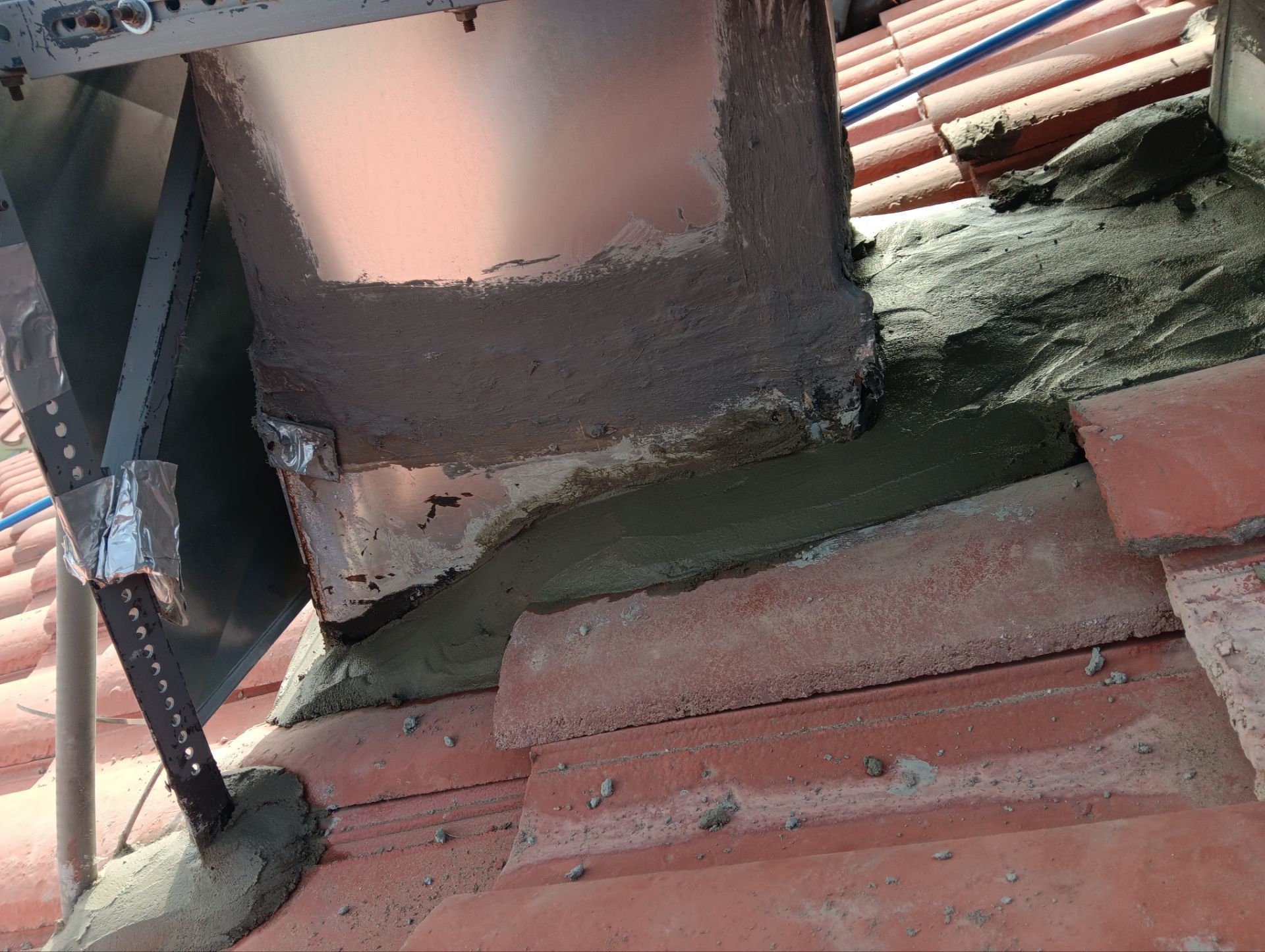 Close-up of a tiled roof with flashing and sealant around a rectangular structure, possibly a vent or solar panel mount.