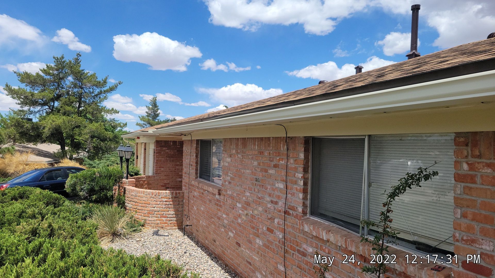 Brick house with white gutters, two windows, and blue sky with clouds.