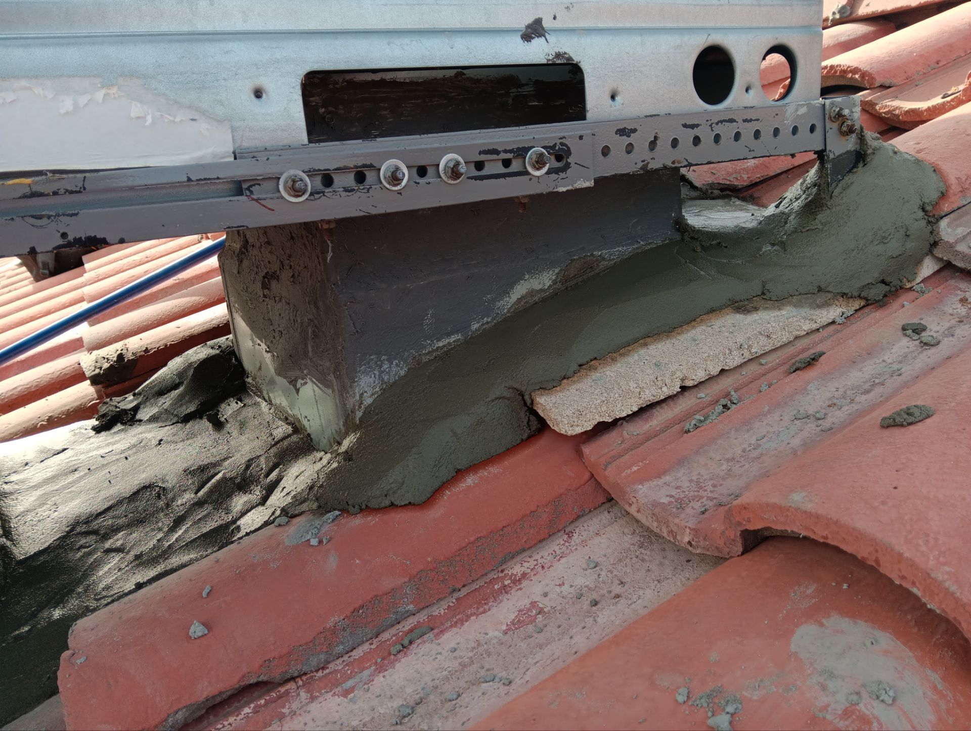 Solar panel mounting bracket secured to a roof with cement and bricks, on red tiles.