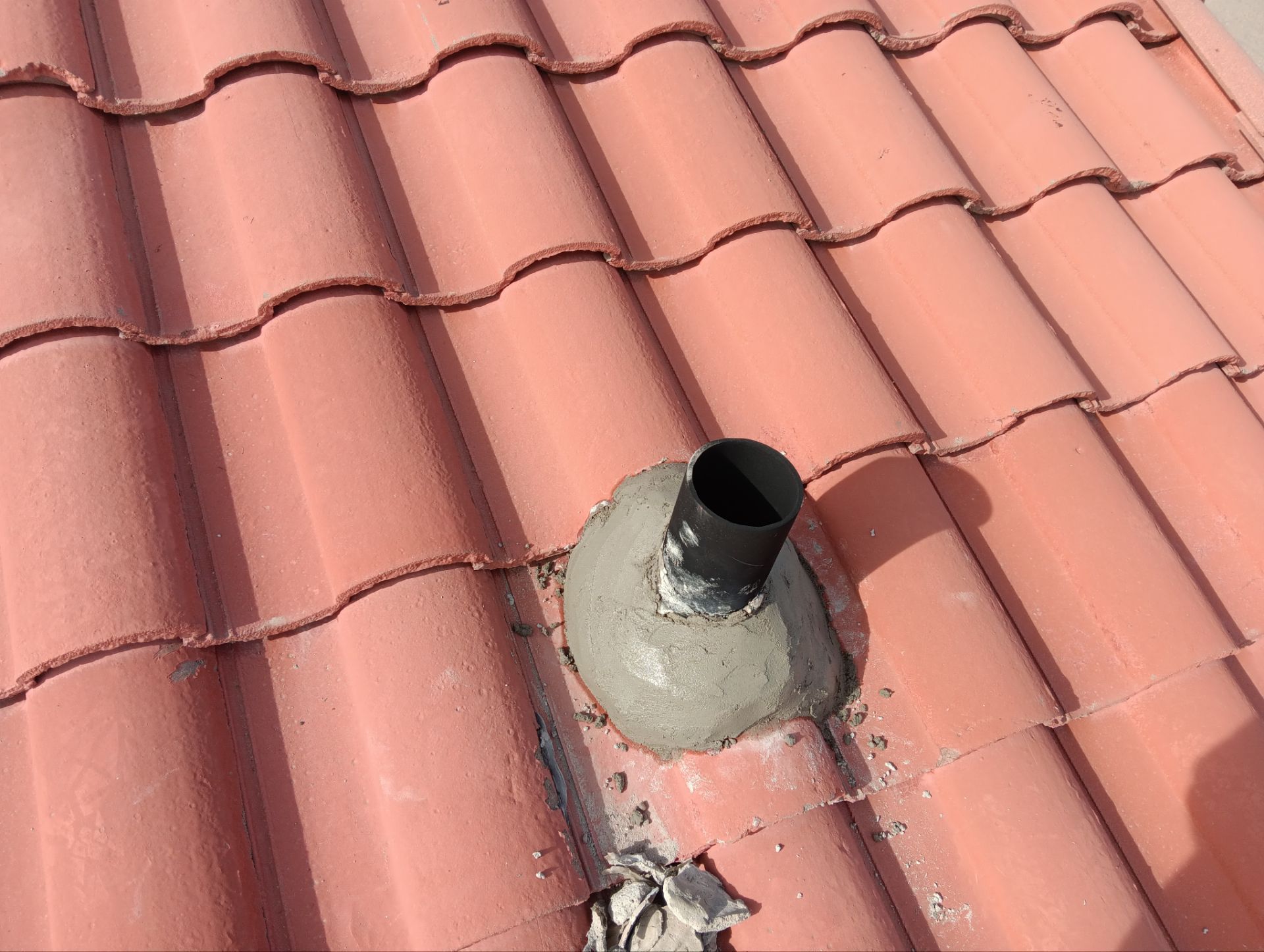 Black pipe protruding from a cement base on a red tile roof.
