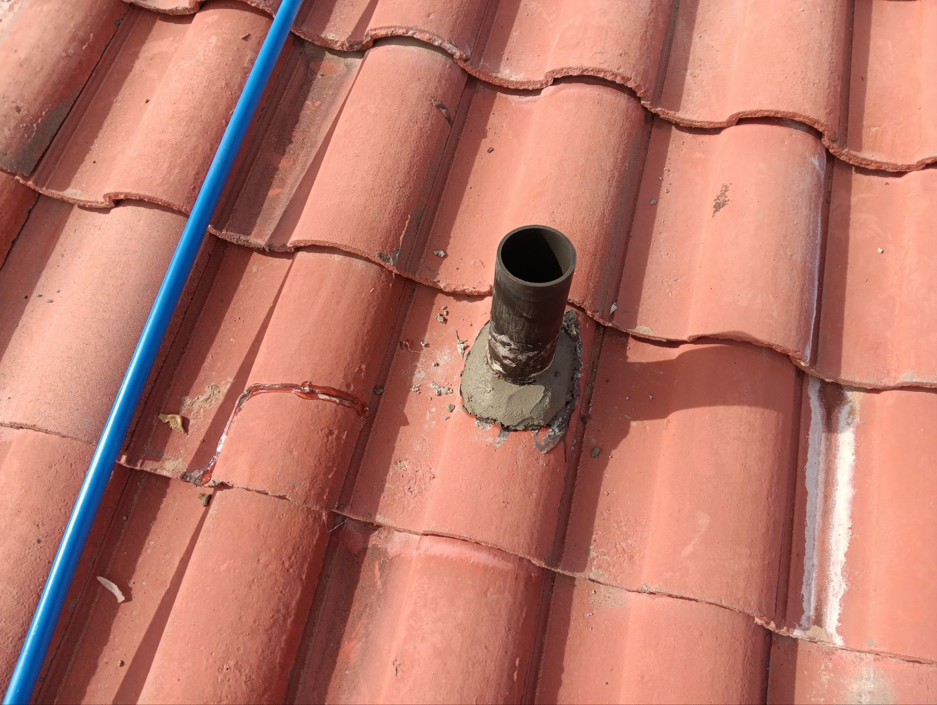 Red tile roof with a black pipe vent sealed with gray sealant.