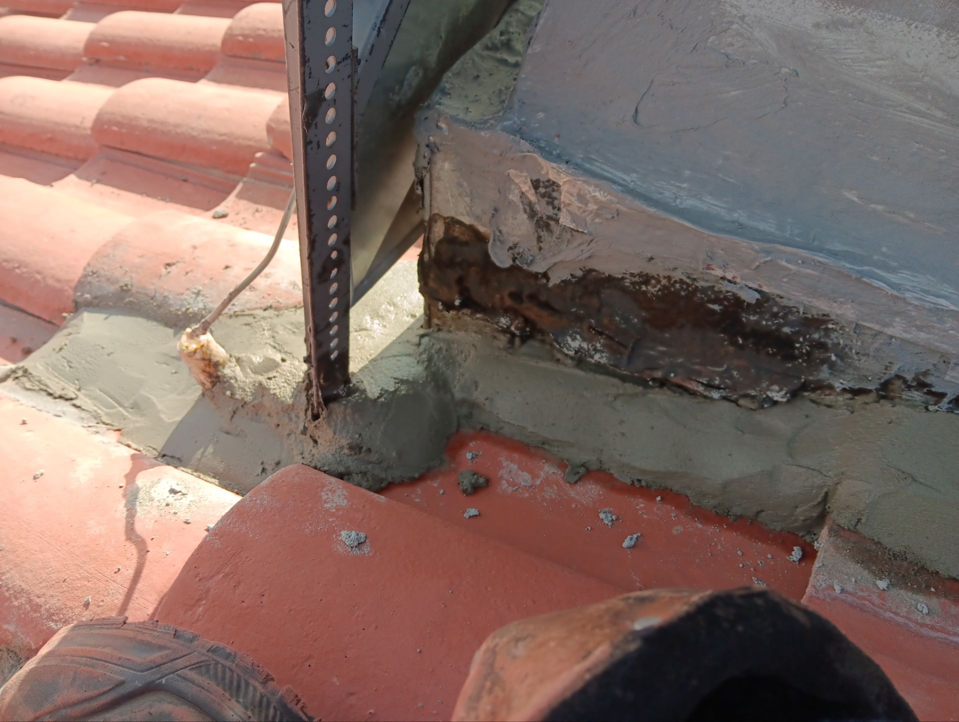 Damaged roof flashing with exposed wood and broken tiles.