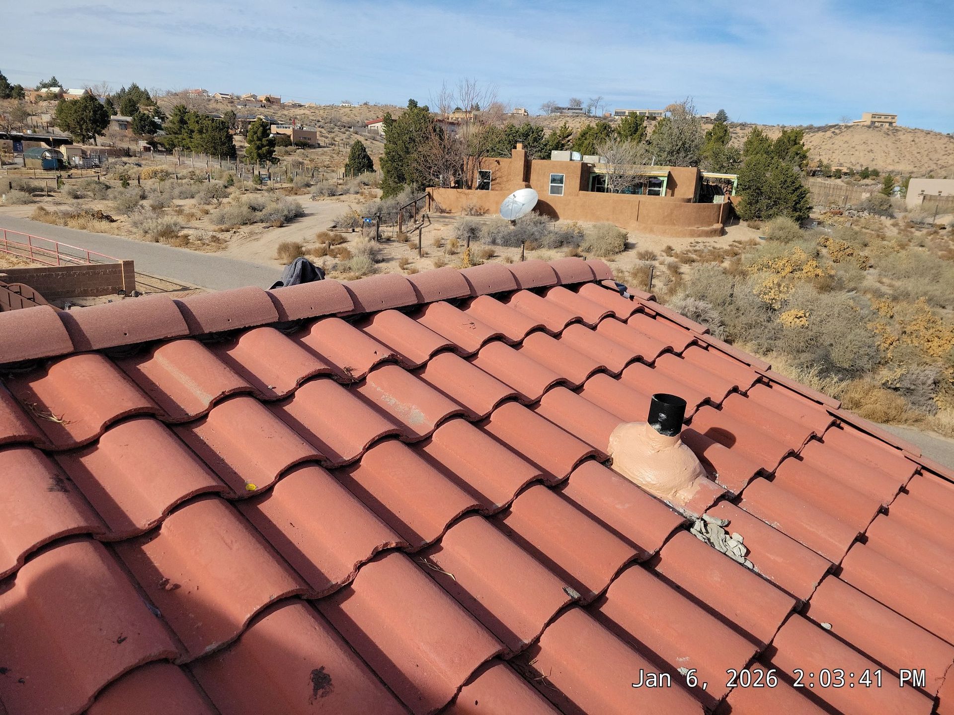 Red tile roof with a desert landscape and a distant adobe building under a blue sky.