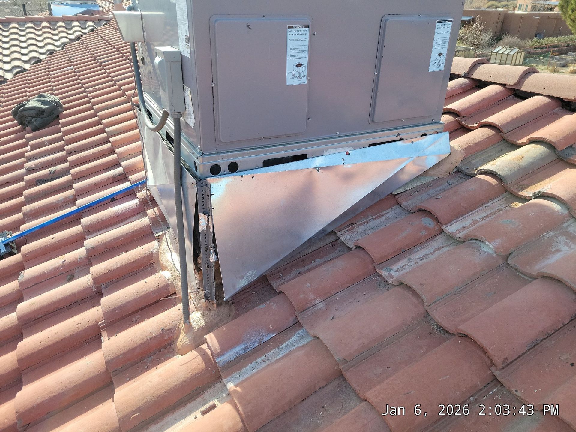 An air conditioning unit on a red tile roof, with some metal flashing attached.