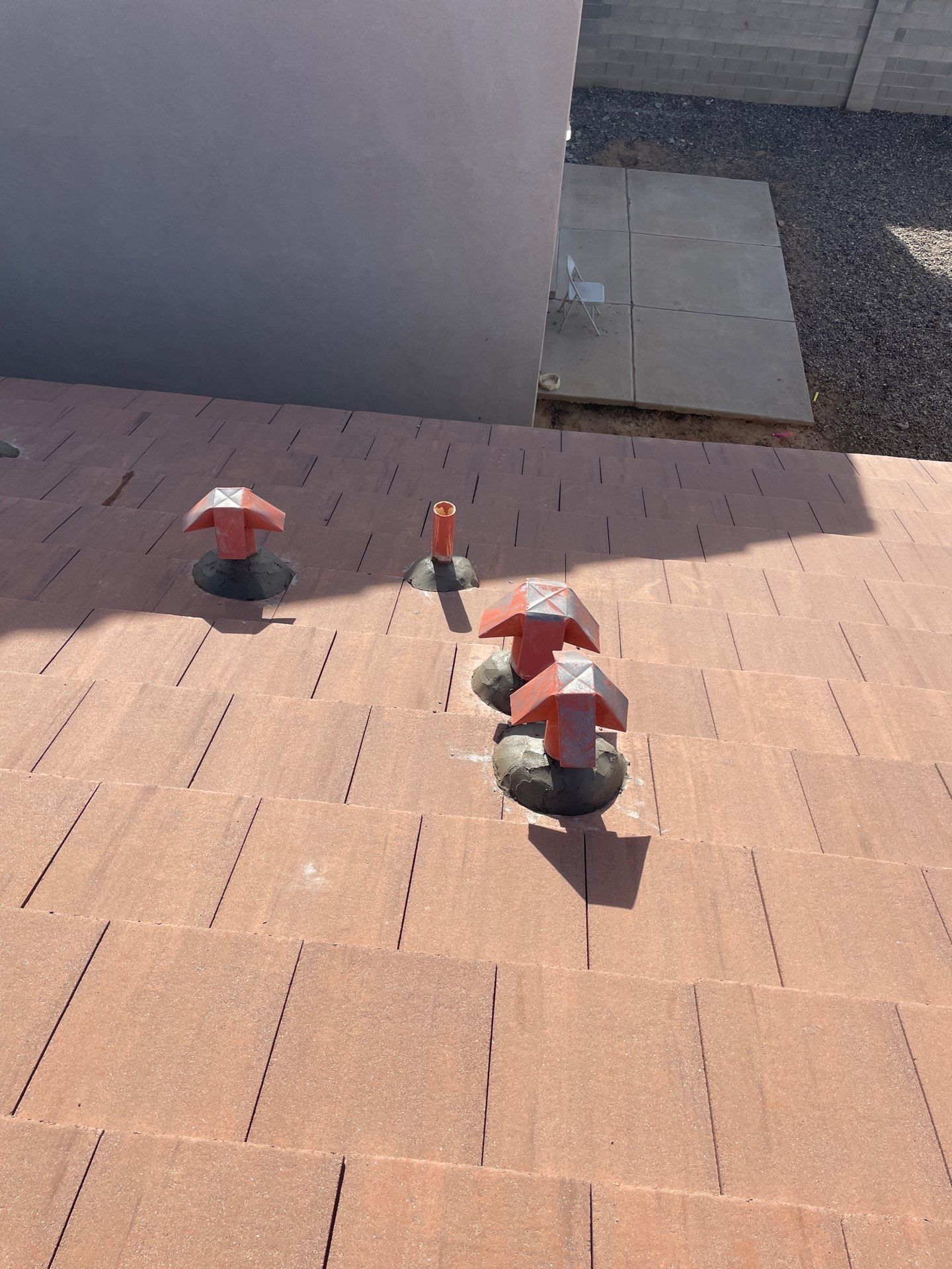Red roof with vents, near a gray wall and concrete path.