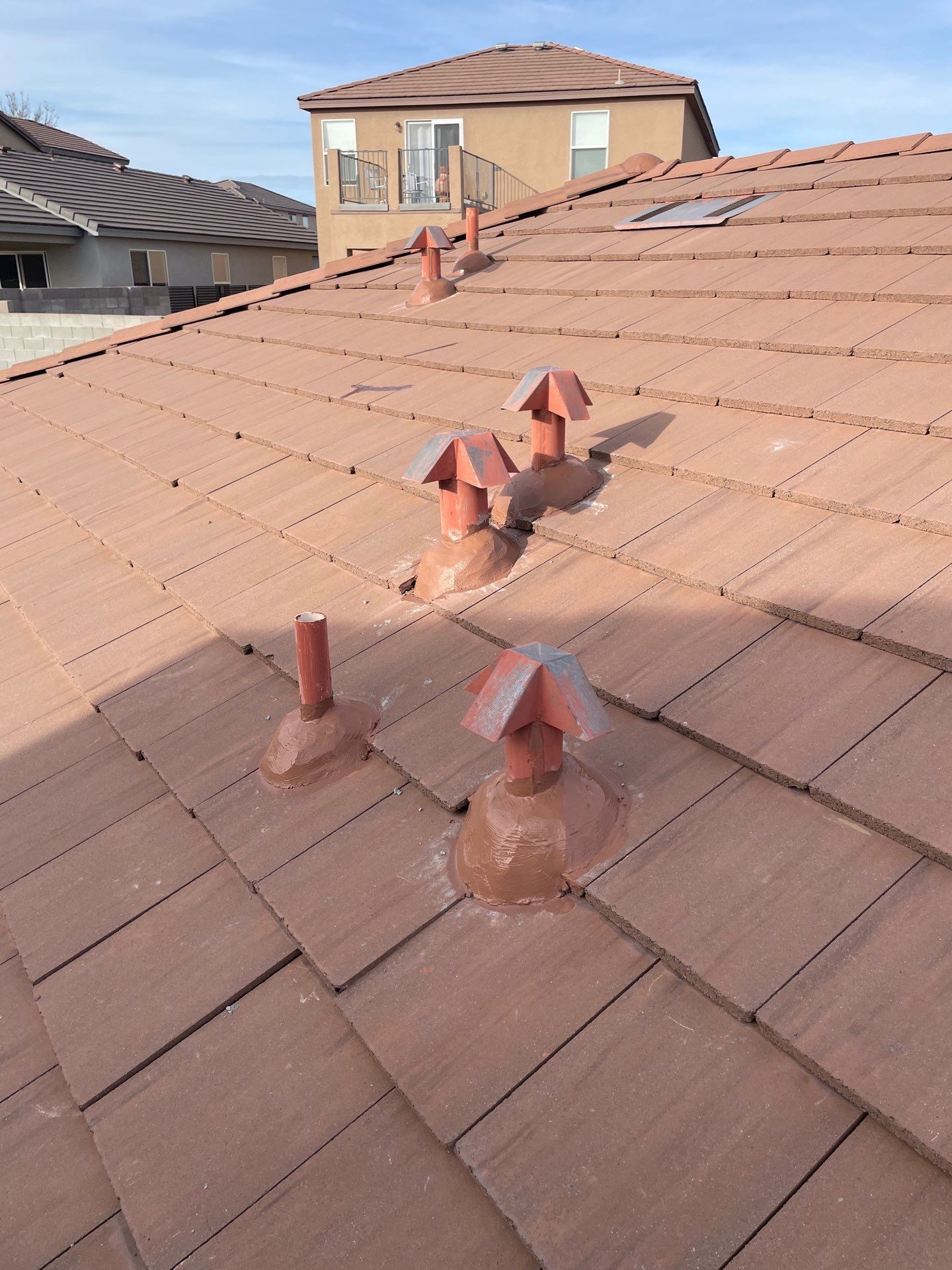 Brown tile roof with several vent pipes, sunny outdoor setting.