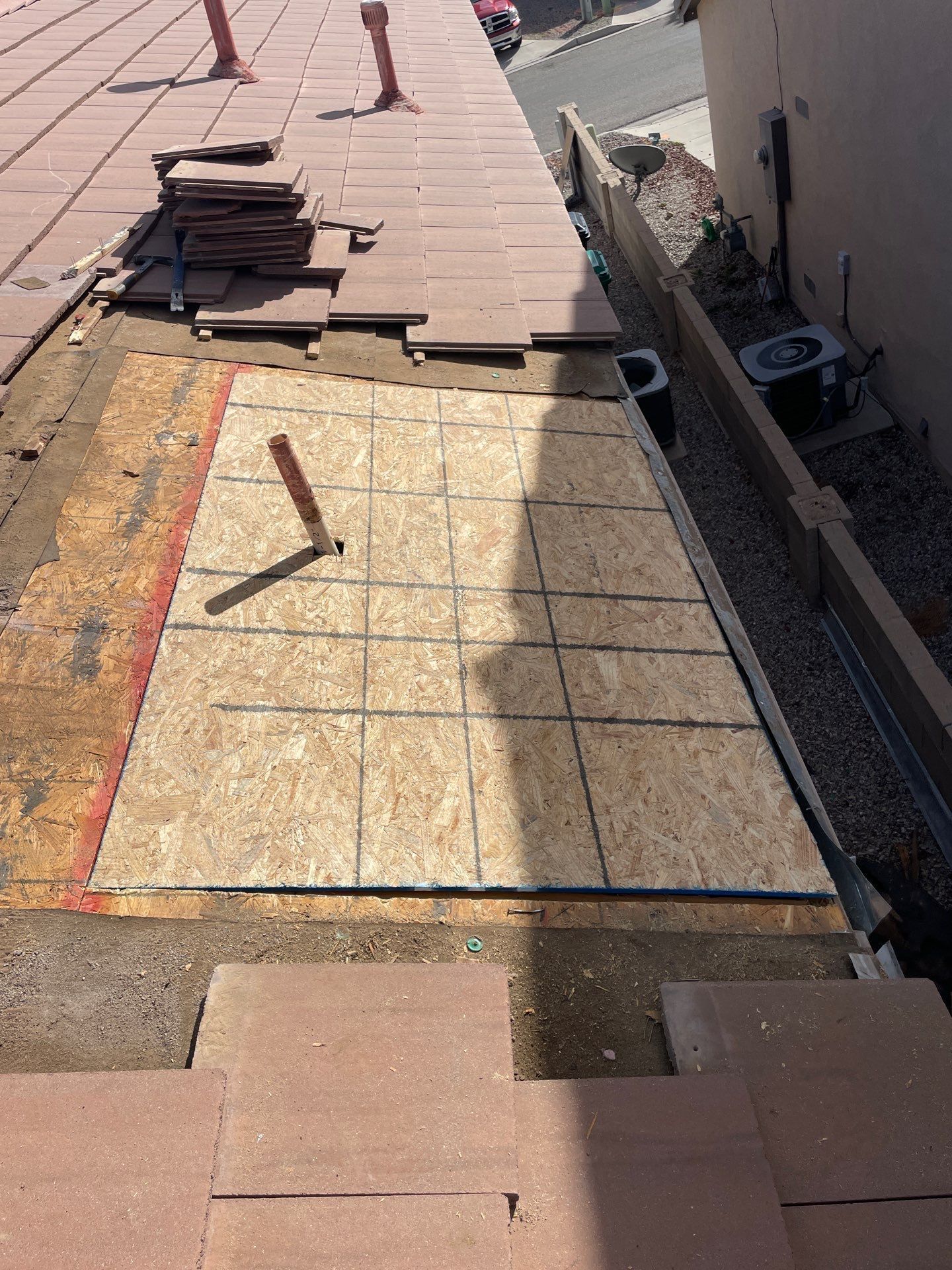 Roof repair in progress: new plywood section replacing damaged area, surrounded by clay tiles.