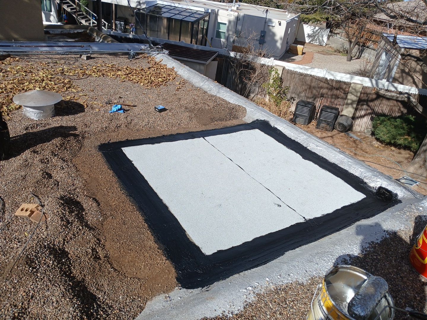 Flat roof with gravel, showing a newly installed white membrane patch, framed by black sealant.