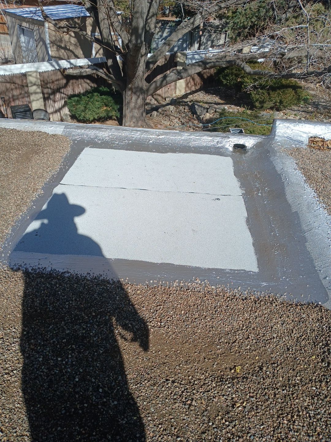 Shadow of person on a gravel roof, centered on a square of lighter material, surrounded by a dark border.