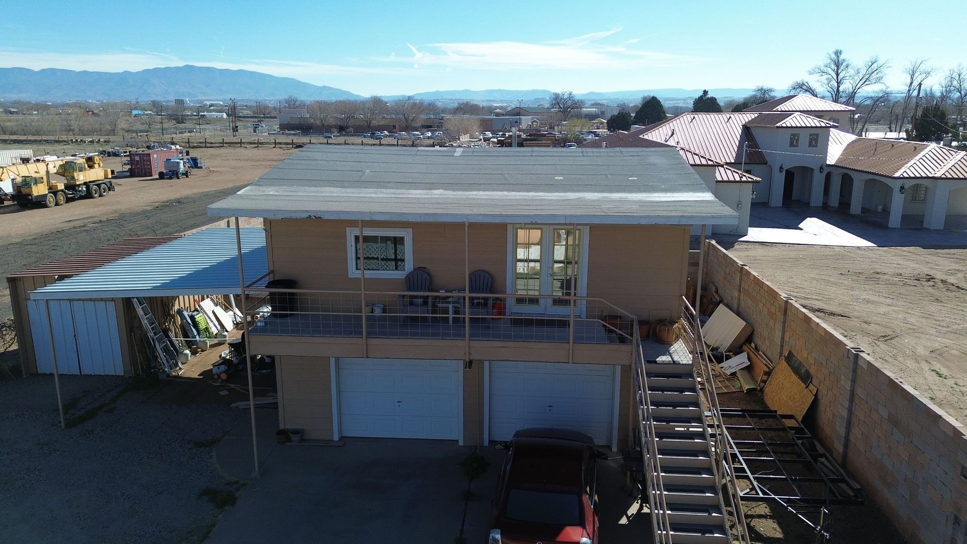 Tan house with two garage doors and a balcony. A red car is parked in front.