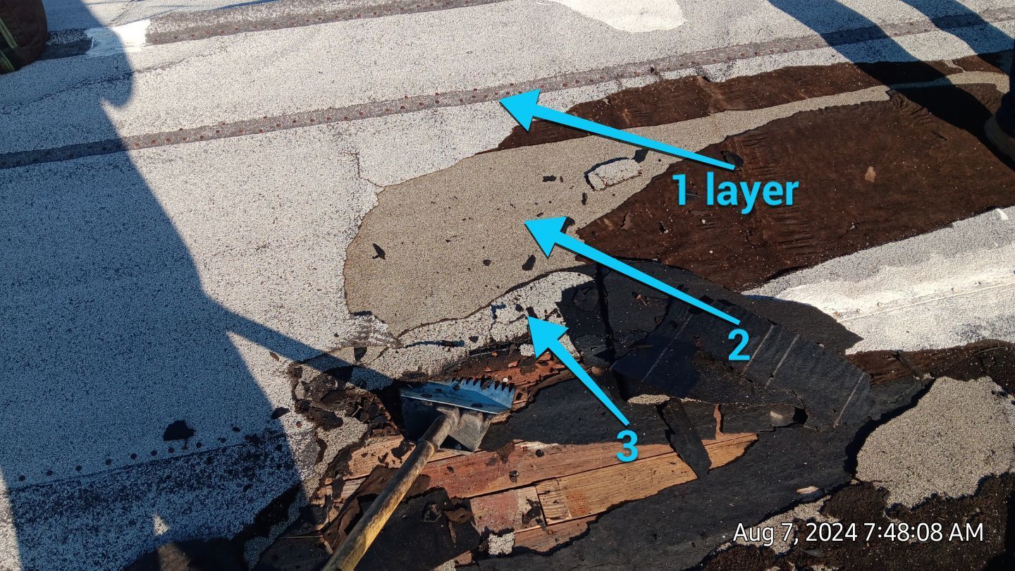 Overhead view of a roof damage. Three layers of materials exposed: gray asphalt, gray, and black.