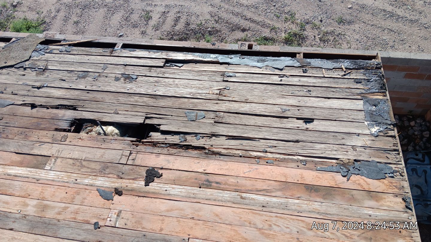 Damaged roof with missing shingles and a visible hole. Brown and black weathered wood.