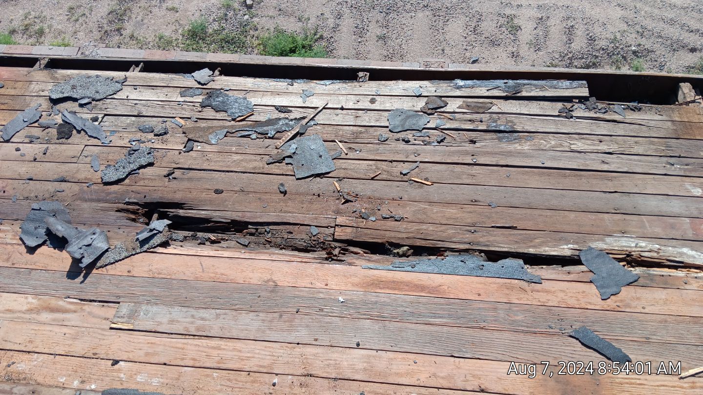 Weathered wooden planks with crumbling dark gray material on top.