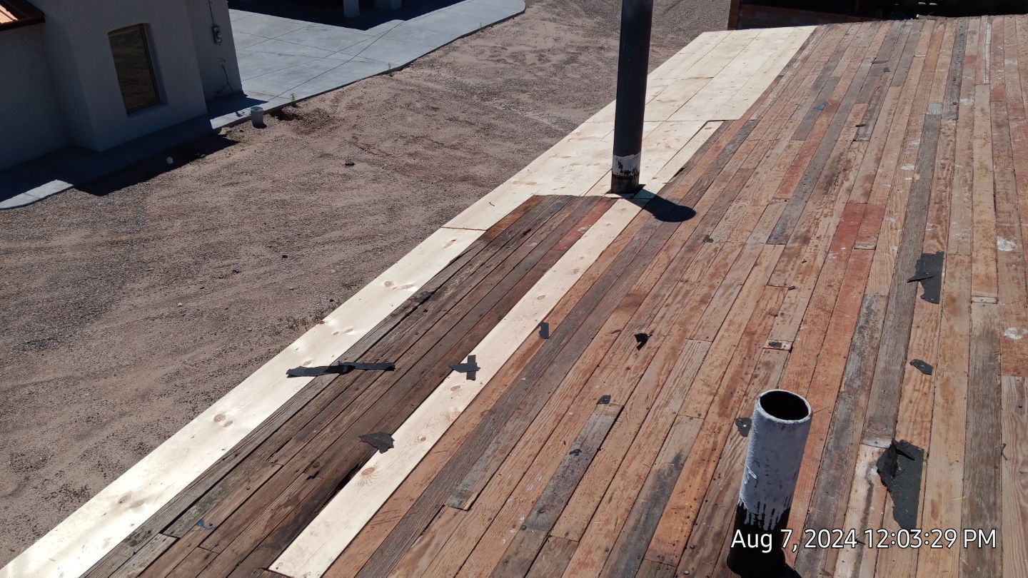 Overhead view of a partially constructed roof with wood planks and a chimney, next to dirt ground.