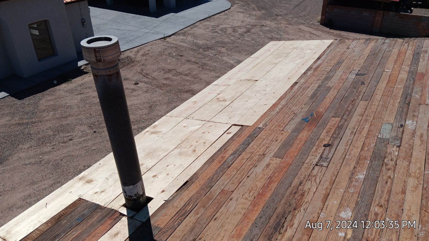 Roof under construction; wooden planks being laid on roof with chimney.