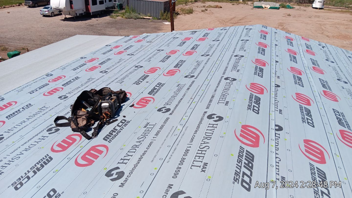 Rooftop with roofing underlayment in progress, tool bag visible. Blue, grey, and red colors. Outdoor setting.