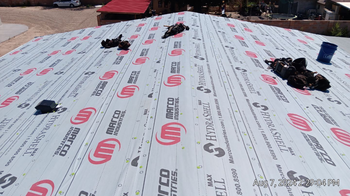 Roof with rolled roofing material in place; tools and supplies scattered on top.