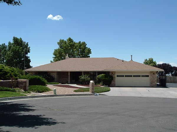 Ranch-style house with tan roof and brick exterior, set on a sunny day with blue sky. Driveway, garage door visible.