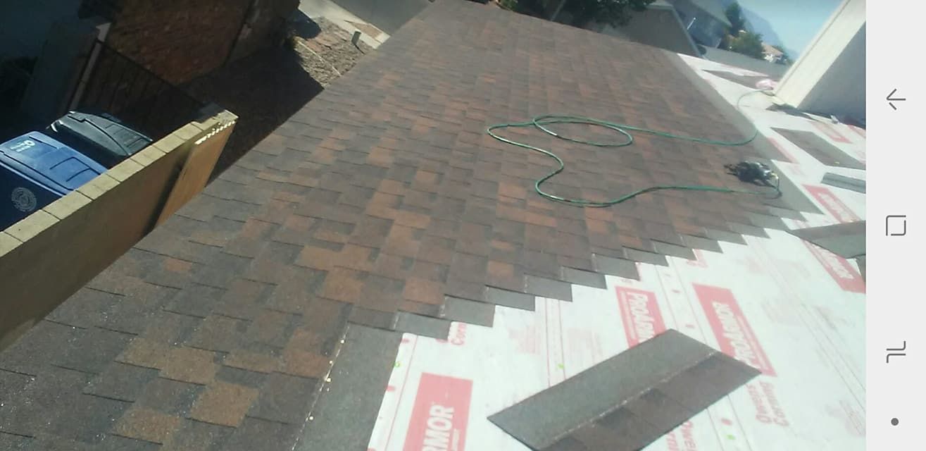 Roofing work in progress, with newly laid brown shingles and underlayment visible. A green hose lays on top of the roof.