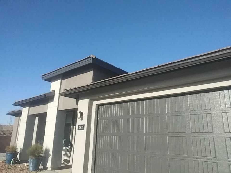 Modern home with gray garage door, beige facade, and dark roof under a clear blue sky.