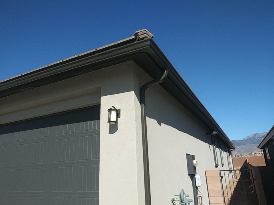 Garage exterior with dark gutter, light stucco walls, and a blue sky.