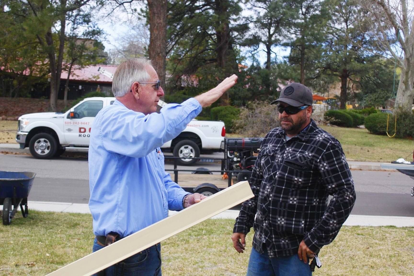 Man in a bright attic leans against a cabinet, talking on the phone and holding a tablet.