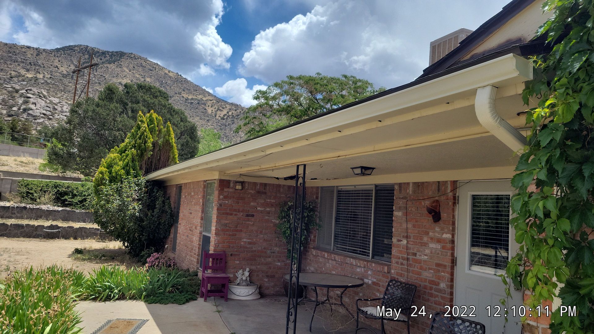 Brick house with a covered porch, mountains in the background, blue sky with clouds.