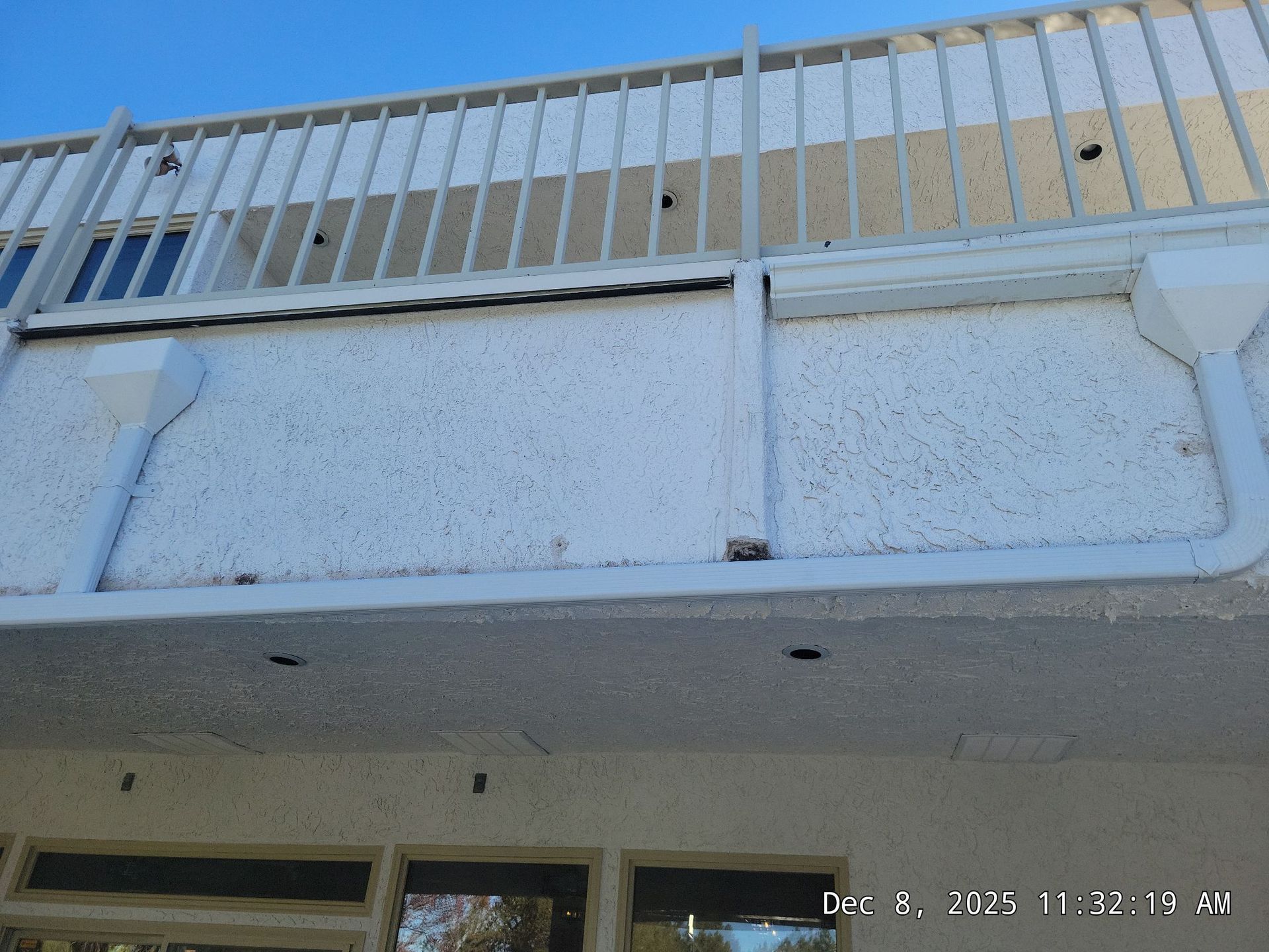 Exterior view of a building with white stucco wall and railing, with a blue sky background.