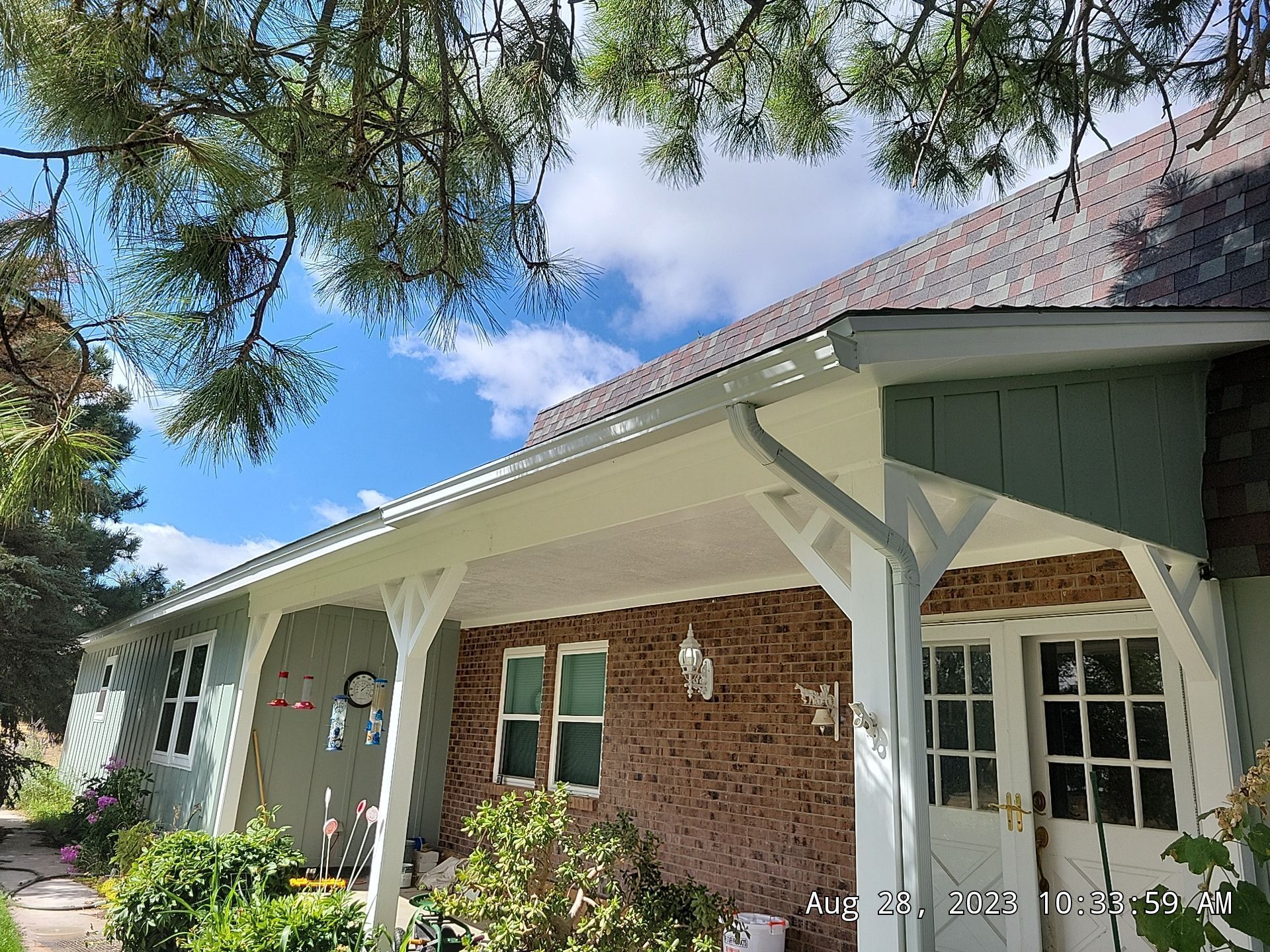 A light green house with a covered porch under a bright sky, surrounded by greenery.