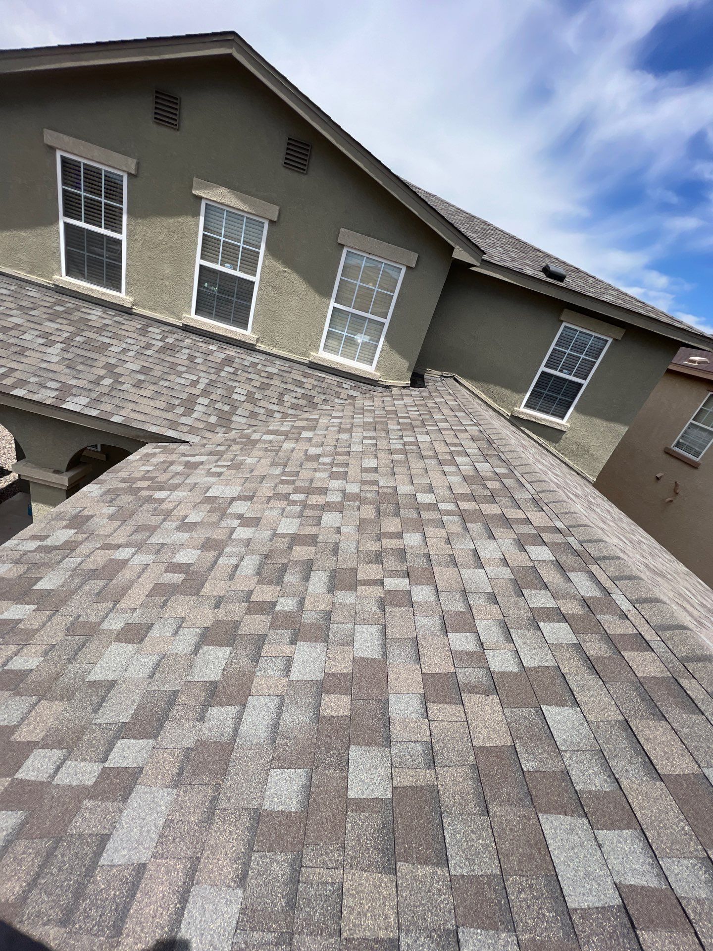 View of a house roof with various shades of gray shingles against a blue sky.