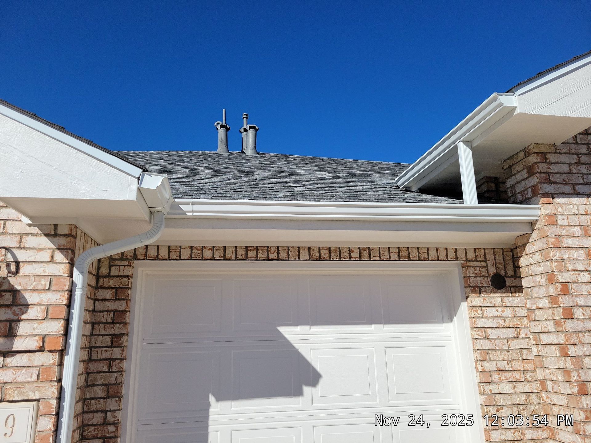 Garage with white door, brick exterior, white gutters, and gray roof against a blue sky.
