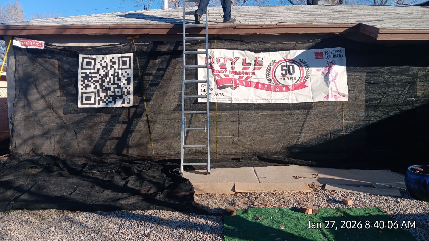 Person on a ladder, working on a building with a large QR code and banner. Black mesh covers the facade.