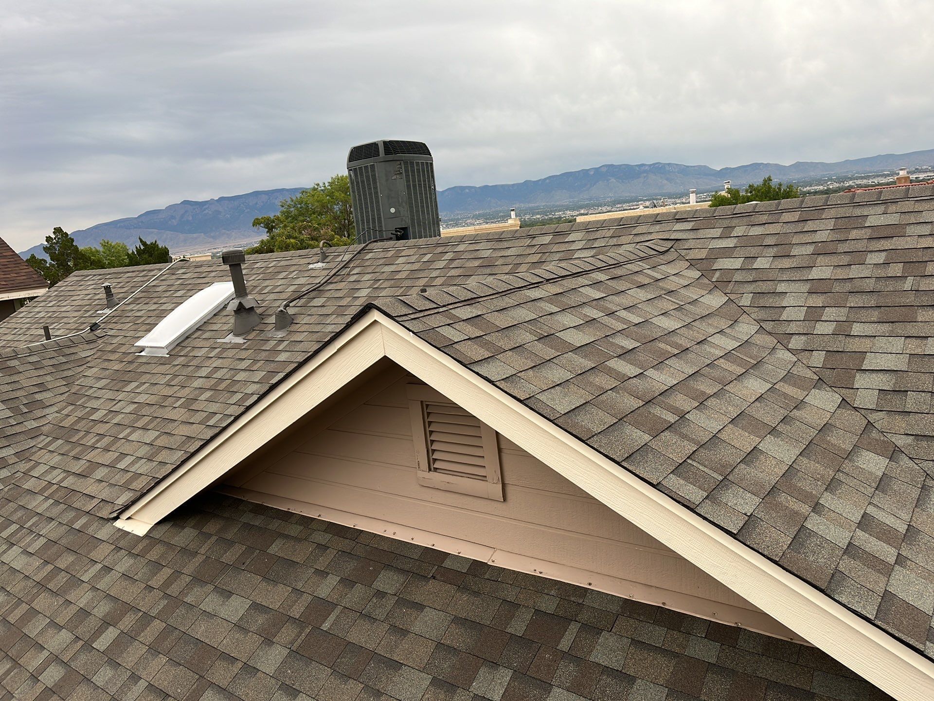 Roof with shingles, chimney, and gable, overlooking a landscape under a cloudy sky.